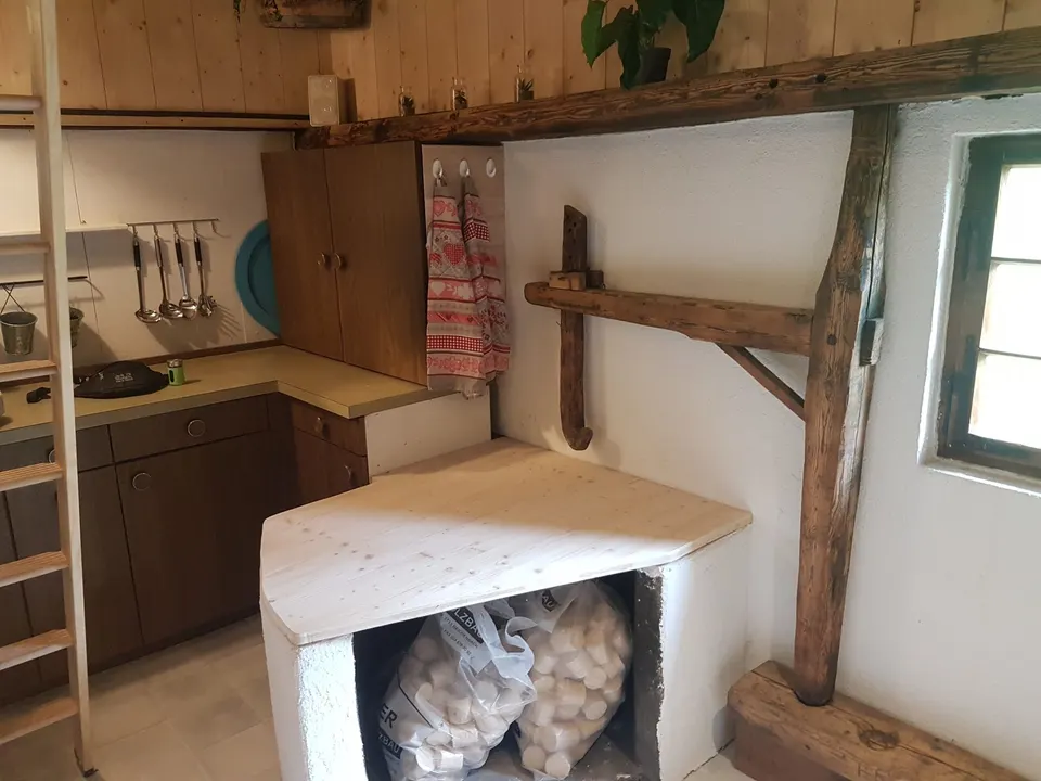 Küchenecke mit Arbeitsfläche, Schränken und gemauerter Ablage, darunter Holzbriketts