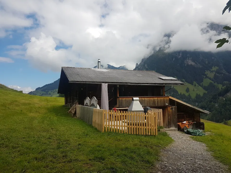 Hütte im Sommer mit eingezäunter Terrasse und Gartencheminée, Kiesweg zum Eingang